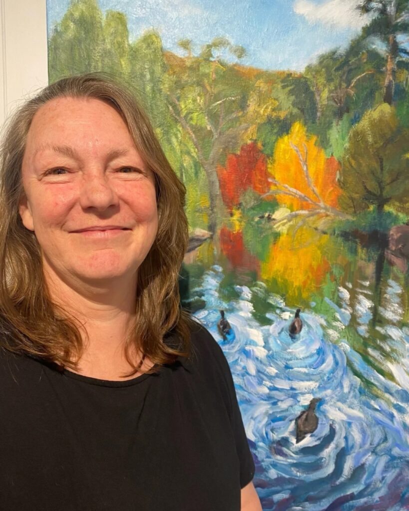 Jodie Kilmister standing beside her painting of ducks on water in a vibrant landscape setting