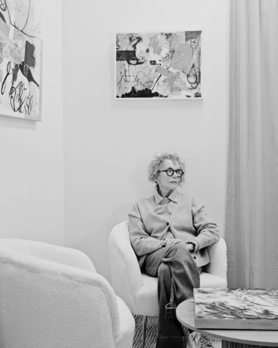 Black-and-white portrait of artist Sally Beresford seated in a gallery space surrounded by contemporary artworks.